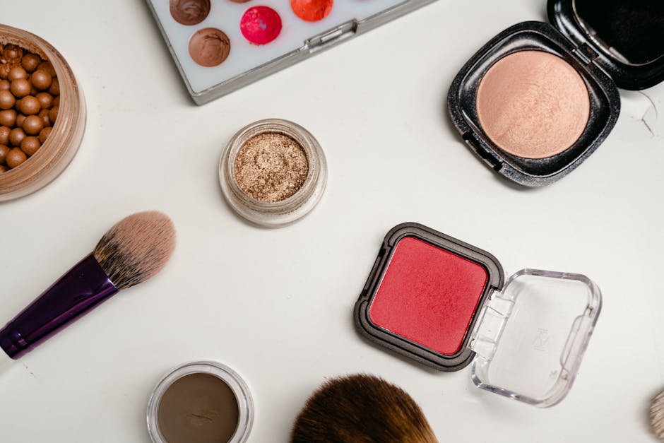 Flat lay raznih makeup proizvoda uključujući četkice, pudere i kreme na bijeloj površini