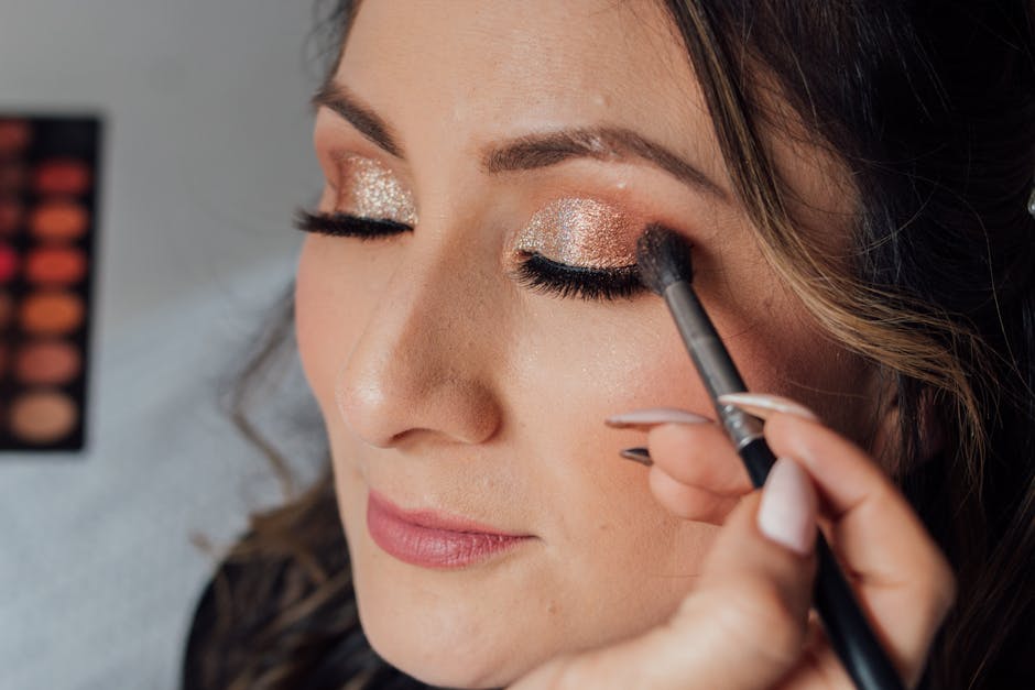 Woman receiving glamorous makeup with glitter eyeshadow and long lashes.